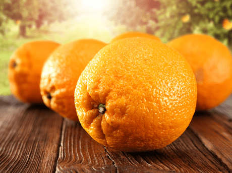 fünf frische Orangen auf einem dunklen Holztisch im Garten