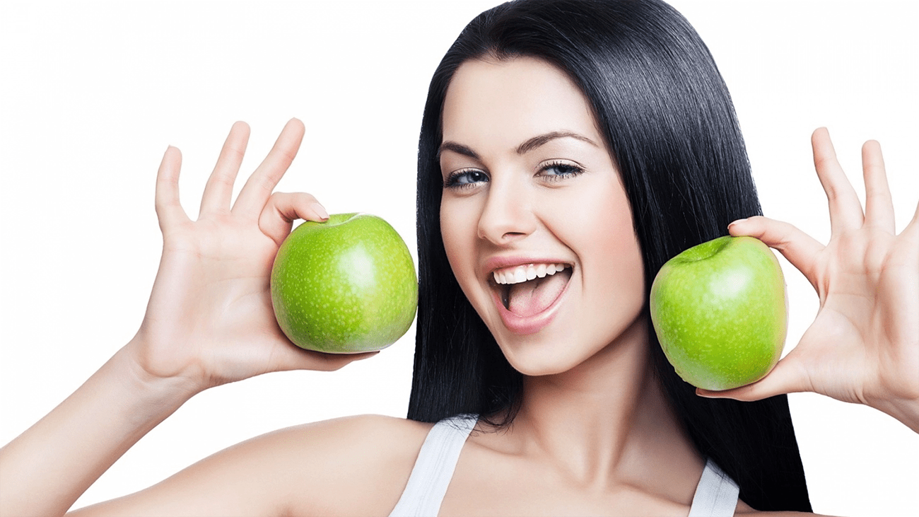 lächelndes schwarzhaariges Mädchen mit zwei grünen Äpfeln
